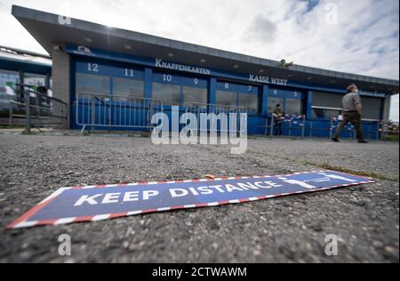 25 settembre 2020, Renania Settentrionale-Vestfalia, Gelsenkirchen: Un uomo è in piedi presso una biglietteria aperta di fronte alla Veltins-Arena, lo stadio di Schalke 04, mentre sul pavimento c'è un cartello che dice 'Keep Distance'. Alla luce delle ultime cifre relative all'infezione da corona, il primo gioco in casa del club tedesco Bundesliga FC Schalke 04 di questo sabato potrebbe essere giocato di fronte ai tifosi. Il numero rilevante di persone recentemente infettate negli ultimi sette giorni ogni 100,000 abitanti è sceso al di sotto della soglia di divieto dal 35 al 33.4. Le autorità sanitarie della città hanno l'ultima parola. Foto: Bernd Thissen/dpa - IMPORT Foto Stock