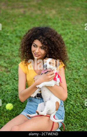 Fuoco selettivo della giovane donna seduta sull'erba con il cane e guardando via Foto Stock