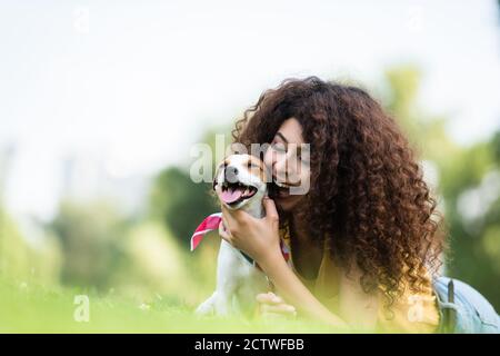 fuoco selettivo di eccitato, donna riccia hugging jack russell terrier cane mentre si sdraia su erba Foto Stock