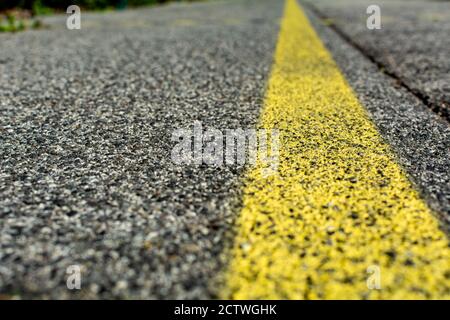 Struttura di asfalto granulare. Primo piano di una texture di Asphalt con una linea gialla di marcatura stradale. Fondo stradale astratto. Foto Stock