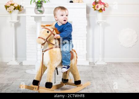 bambino in pullover blu e jeans si siede su un cavallo giocattolo. Non gli piace quello che sta succedendo. Disgusto, loathing Foto Stock