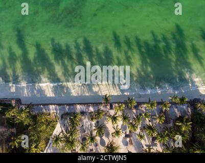 Foto aerea di un hotel di lusso su una spiaggia prima La linea con gli alberi di palma cade le loro tonalità su un alto Marea acqua dell'Oceano Indiano alla sera in Paje Foto Stock