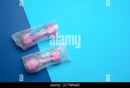 un paio di manubri viola sportivi in una borsa trasparente su sfondo blu, vista dall'alto, spazio copia Foto Stock