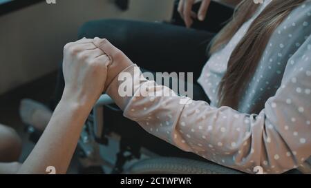 Primo piano, mano che tiene la mano della giovane donna che si recupera in sedia a rotelle. Foto di alta qualità Foto Stock