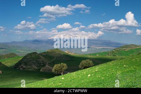 Paesaggio primaverile della campagna siciliana intorno all'Etna con casa rurale, campo di erba verde sotto le nuvole bianche Foto Stock