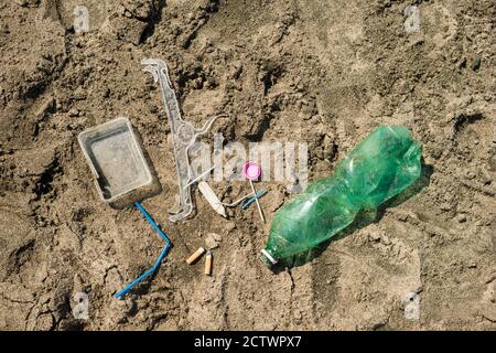 Verde, bottiglia di plastica, bastoncini di cotone, tappo, scatola e sigarette lasciati su una spiaggia di sabbia. Foto Stock