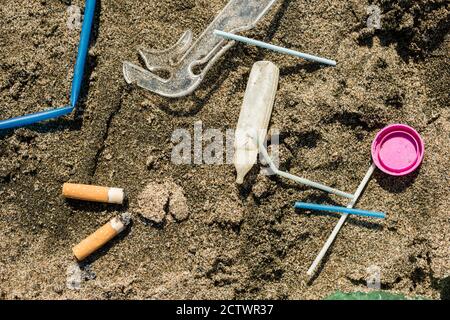 Verde, bottiglia di plastica, bastoncini di cotone, tappo, scatola e sigarette lasciati su una spiaggia di sabbia. Foto Stock