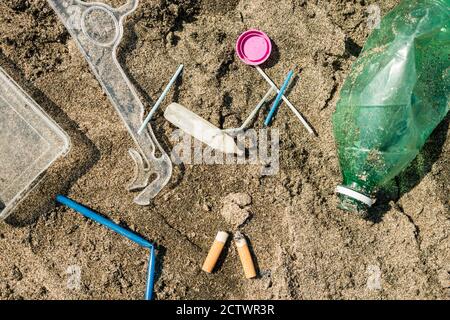 Verde, bottiglia di plastica, bastoncini di cotone, tappo, scatola e sigarette lasciati su una spiaggia di sabbia. Foto Stock