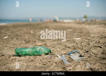 Verde, bottiglia di plastica, bastoncini di cotone, tappo, scatola e sigarette lasciati su una spiaggia di sabbia. Foto Stock