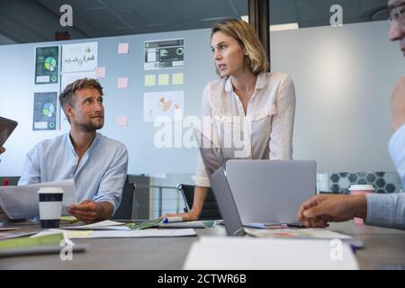 Donna d'affari caucasica in piedi per rivolgersi ai colleghi durante una riunione di squadra, una collega maschio caucasica seduta accanto al suo ascolto. Busine creativo Foto Stock