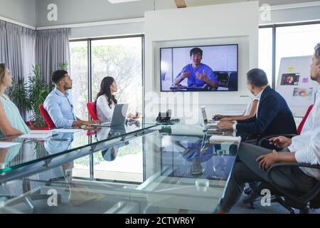 Gruppo multietnico di colleghi di lavoro di sesso maschile e femminile che si trovano in videoconferenza con un collega asiatico di sesso maschile che parla sullo schermo. Affari creativi Foto Stock
