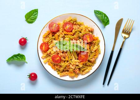 Fusilli - classica pasta italiana di grano duro con carne di pollo, pomodori ciliegia, basilico in salsa di pomodoro in ciotola bianca su tavola di legno blu Foto Stock