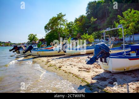 Vista sul mare calmo e sulla spiaggia di sabbia ciottolosa, le barche da pesca sono ormeggiate a secco. Foto Stock