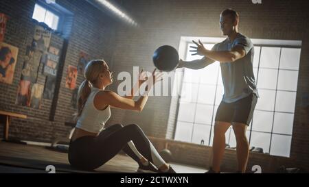 Bella giovane ragazza esercizi con Personal Trainer, facendo seduta-up con palla di Medicina, gettando Passo avanti e indietro. Allenamento in coppia forte e in forma Foto Stock