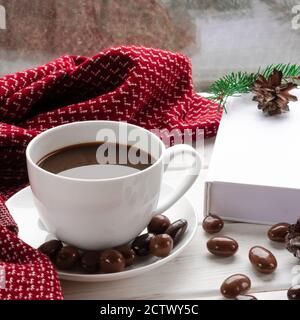 Tazza di caffè bianco con cioccolatini su un bianco soglia del finestrino contro il finestrino Foto Stock