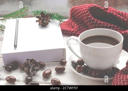 Tazza di caffè bianco con cioccolatini su un bianco soglia del finestrino contro il finestrino Foto Stock