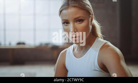 Primo piano Ritratto della bella strong Fit Blonde seduta in una Loft Industrial Gym con Posters Motivational. Sta catturando il suo respiro dopo intenso Foto Stock