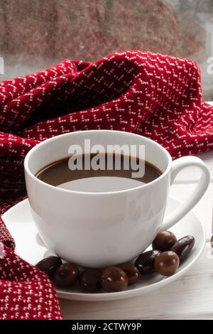 Tazza di caffè bianco con cioccolatini su un bianco soglia del finestrino contro il finestrino Foto Stock