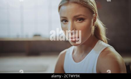 Primo piano Ritratto della bella strong Fit Blonde seduta in una Loft Industrial Gym con Posters Motivational. Sta catturando il suo respiro dopo intenso Foto Stock