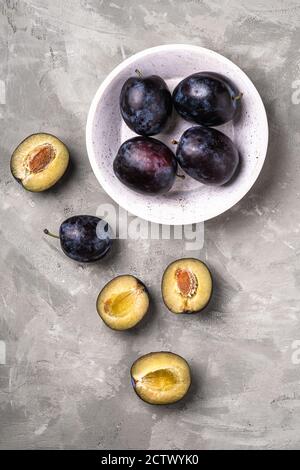 Frutta fresca di prugne matura intera e tagliata in ciotola di legno, fondo in pietra di cemento, vista dall'alto Foto Stock