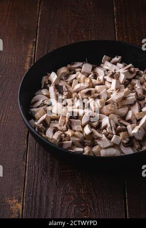 Gustosi funghi champignon tritati in padella, cibi non cotti a fette, sfondo di legno marrone scuro, vista angolare Foto Stock