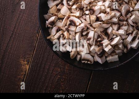 Gustosi funghi champignon tritati in padella, cibi cotti a fette, sfondo di legno marrone scuro, vista dall'alto Foto Stock