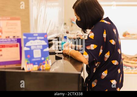 Donna anziana in maschera protettiva firma carta di credito in negozio di abbigliamento. Foto Stock