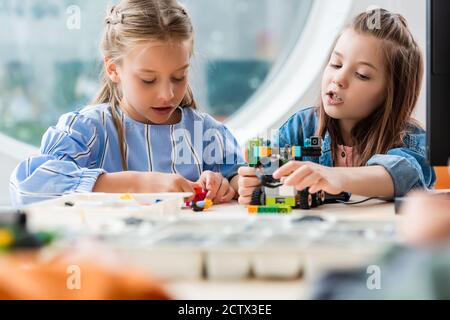 Fuoco selettivo della studentessa che costruisce il robot vicino all'amico in stelo scuola Foto Stock