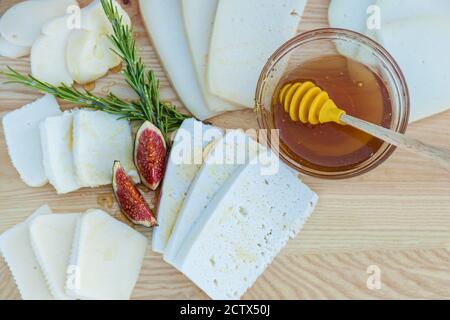 Formaggio tritato di diverse varietà annaffiato con miele, fichi e una tazza con miele su fondo di legno Foto Stock