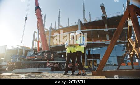 Due specialisti ispezionano il sito di costruzione di edifici industriali e commerciali. Progetto immobiliare con ingegnere civile, investitore uso laptop. Nella Foto Stock