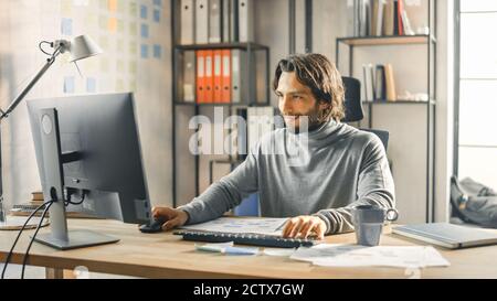 Imprenditore creativo seduto alla sua scrivania funziona su computer desktop nell'elegante ufficio. Bell'uomo ispanico dai capelli lunghi con gli usi di aspetto artistico Foto Stock