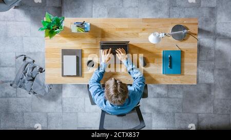 Top View Shot: Uomo d'affari seduto alla scrivania in legno funziona su un computer portatile nel suo ufficio di casa. Scrive e-mail, naviga su Internet, progetta Foto Stock