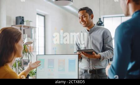 Tre sviluppatori di software mobili lavorano su un computer desktop, parlano di progettazione di applicazioni per smartphone utilizzare il touch screen Digital Tablet. Moderno ed elegante Foto Stock