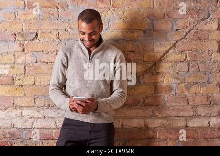 Un felice bel giovane utilizzando il suo smartphone in un maglione. Foto Stock