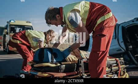 Sull'automobile Crash incidente stradale scena: Paramedici e pompieri soccorrano vittima ferita intrappolata nel veicolo. Estricare la persona usando Stretchers Foto Stock