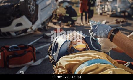 Sull'automobile Crash incidente di traffico scena: Paramedics che salva la vita di una vittima di incidente di traffico che sta mentendo su Stretchers. Ascoltano un Heartbeat Foto Stock