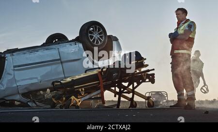 Triste, doloroso Paramedic in piedi alla scena del terribile incidente stradale di incidente stradale di incidente d'arresto auto. Le vittime dell'incidente non sono sopravvissute, non poteva essere sicuro Foto Stock