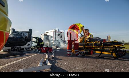 Sulla scena di incidente di traffico di arresto dell'automobile: Paramedics che salva la vita di una ragazza piccola che si trova sugli Stretchers, s ha dato l'aiuto di primo soccorso. Cavi per vigili del fuoco Foto Stock