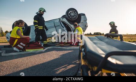 Sull'automobile Crash incidente stradale scena: Paramedici e pompieri soccorrano vittima ferita intrappolata nel veicolo. Estricare la persona usando Stretchers Foto Stock