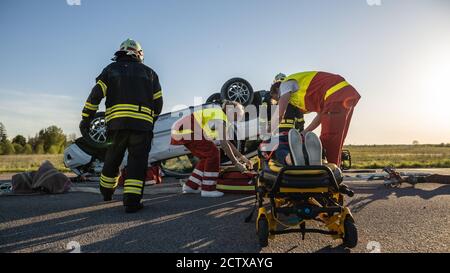 Sull'automobile Crash scena di incidente di traffico: Paramedics che salva la vita di una vittima femminile che sta mentendo su Stretchers. Ascoltano un Heartbeat, si applicano Foto Stock