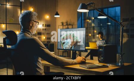 In serata Creative Middle Aged Video Game Developer lavora su un computer desktop con schermo 3D Videogame Level Design. Ufficio professionale Foto Stock