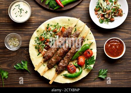 Bagno turco Adana Kebab con verdure fresche su flatbread su sfondo di legno. Vista superiore, laici piatta Foto Stock
