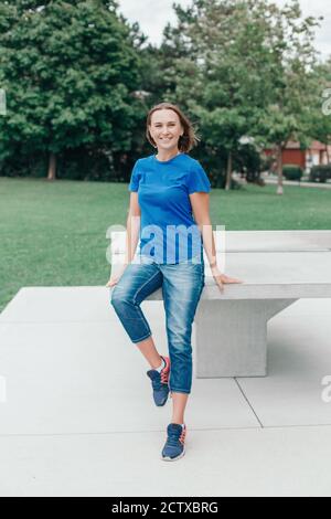 Bella felice sorridente sportivo donna di mezza età in t-shirt blu e jeans parco. Donna caucasica con capello corto nel parco all'aperto. Design sottile e sottile Foto Stock