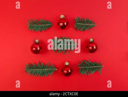 Composizione simmetrica natalizia da baubles giocattolo e rami di abeti su sfondo rosso. Semplice appartamento di festa posato. Foto Stock