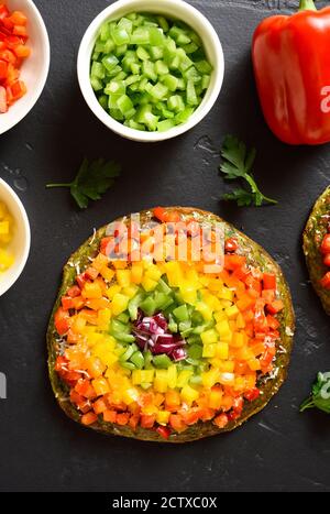 Arcobaleno veggie peperoni pizza campana su fondo di pietra nera. Vegetariano vegano o concetto di cibo sano. Piatto dietetico senza glutine. Vista dall'alto, disposizione piatta Foto Stock