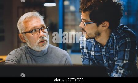 Capo Creative Designer mostra lo schermo del computer desktop a uno sviluppatore giovane, che discute di progetto. Due professionisti che hanno discussione. Scegliere di destra Foto Stock