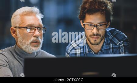 Capo Creative Designer mostra lo schermo del computer desktop a uno sviluppatore giovane, che discute di progetto. Due professionisti che hanno discussione. Scegliere di destra Foto Stock