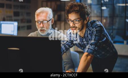 Capo Creative Designer mostra lo schermo del computer desktop a uno sviluppatore giovane, che discute di progetto. Due professionisti che hanno discussione. Scegliere di destra Foto Stock