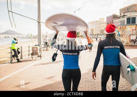 Interessanti gli istruttori di surf giovane a piedi con i loro tavola da surf lungo la passeggiata sul lungomare Foto Stock