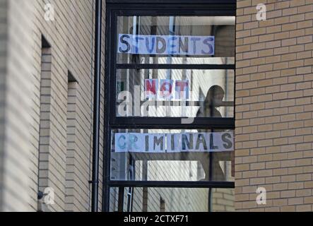 Uno studente passa accanto a un cartello al Murano Street Student Village di Glasgow, dove gli studenti della Glasgow University vengono testati in un centro di test pop-up. Venerdì in Scozia sono entrate in vigore una serie di nuove misure per combattere l'aumento dei casi di coronavirus, tra cui il divieto di visitare le famiglie al coperto e un coprifuoco per pub e ristoranti. Foto Stock